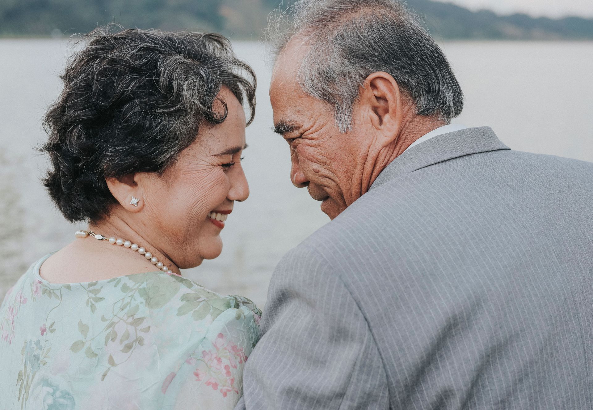 Older couple smiling at each other by a calm waterfront