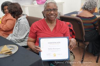 A woman is sitting at a table holding a certificate.