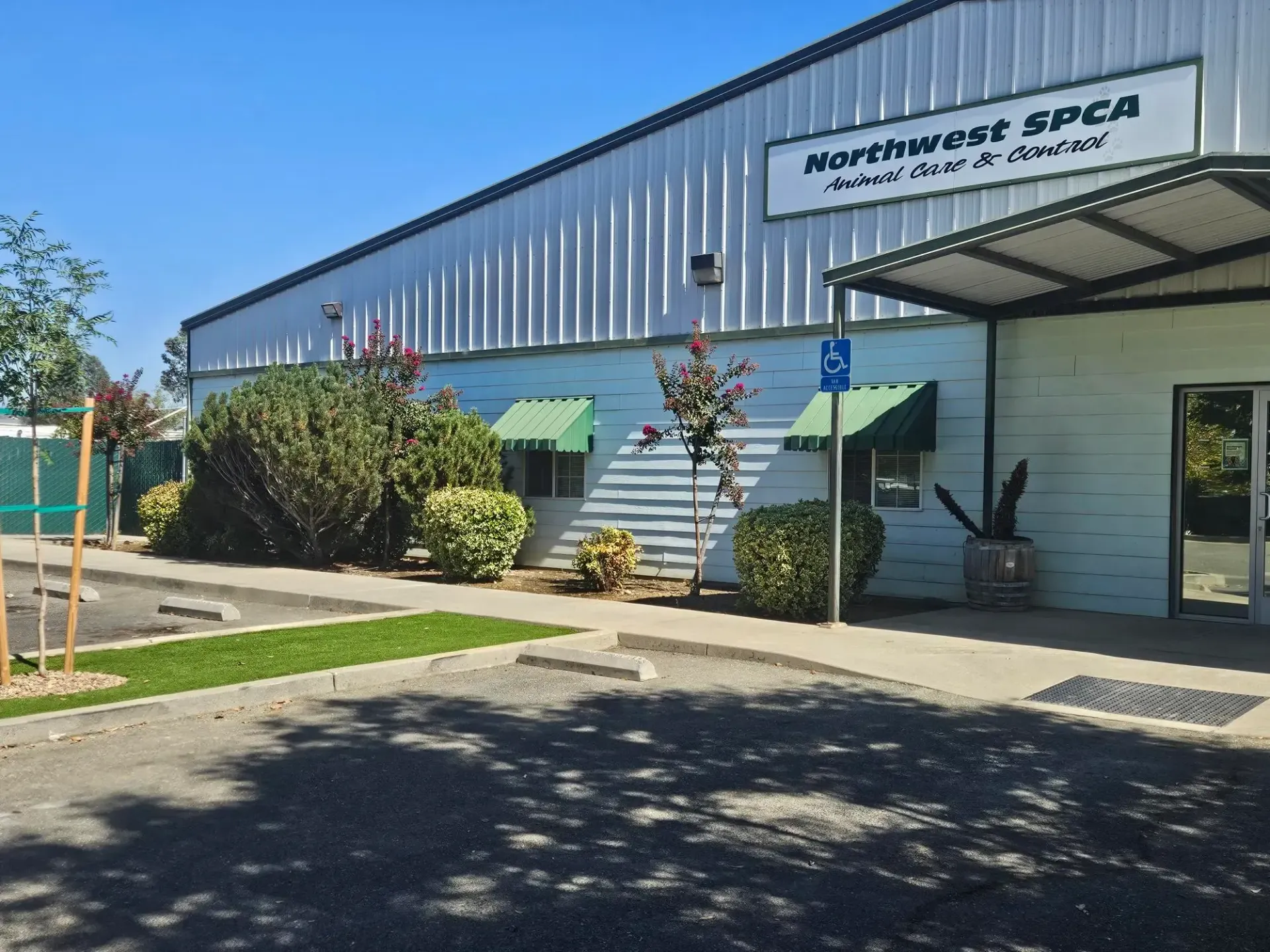 Modern metal building with a sign, awning entrance, and landscaped parking lot in sunlight
