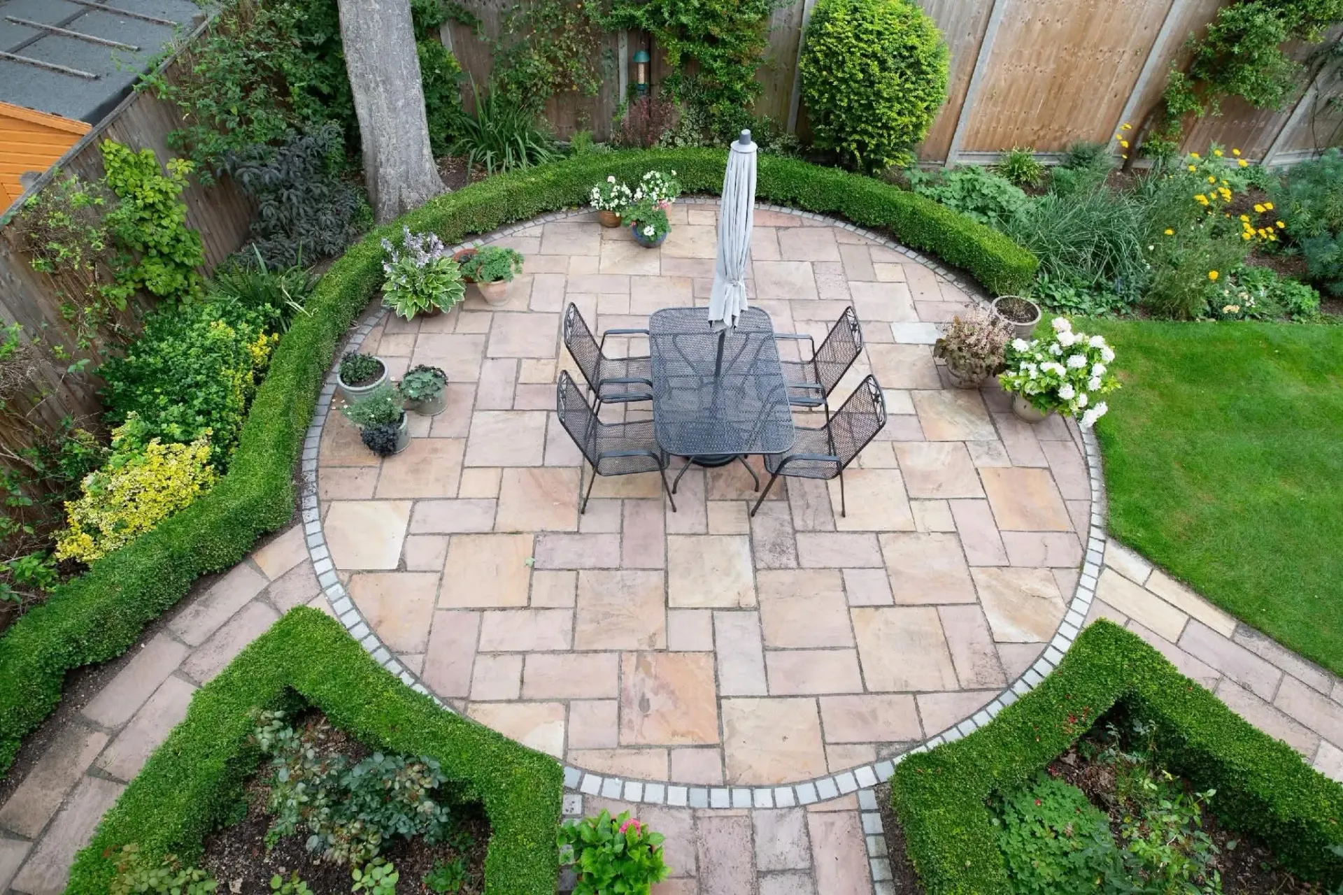 Backyard patio with a fire pit, stone pavers, and surrounding garden beds
