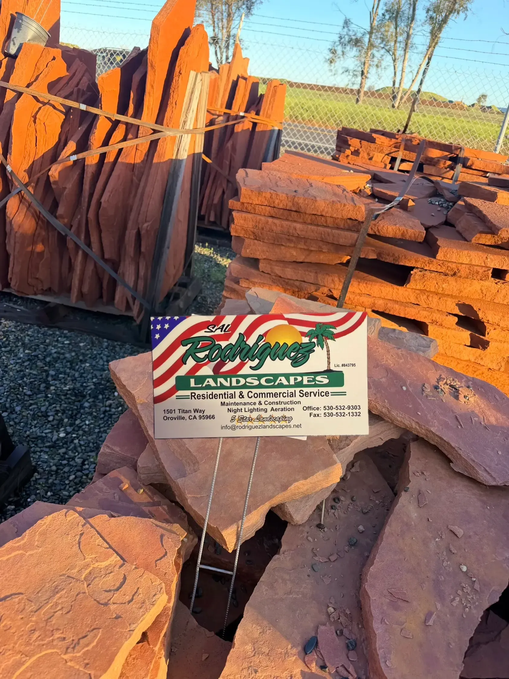 Box of LANDSCAPES firewood and reddish stone pavers stacked outdoors near a field
