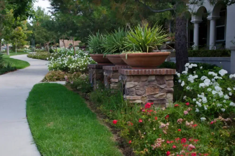 Landscaped garden with curved walkway, stone planter, and colorful flowers beside a house