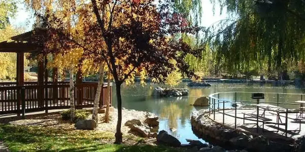 Autumn lakeside park with gazebo, trees, and a circular dock on calm water