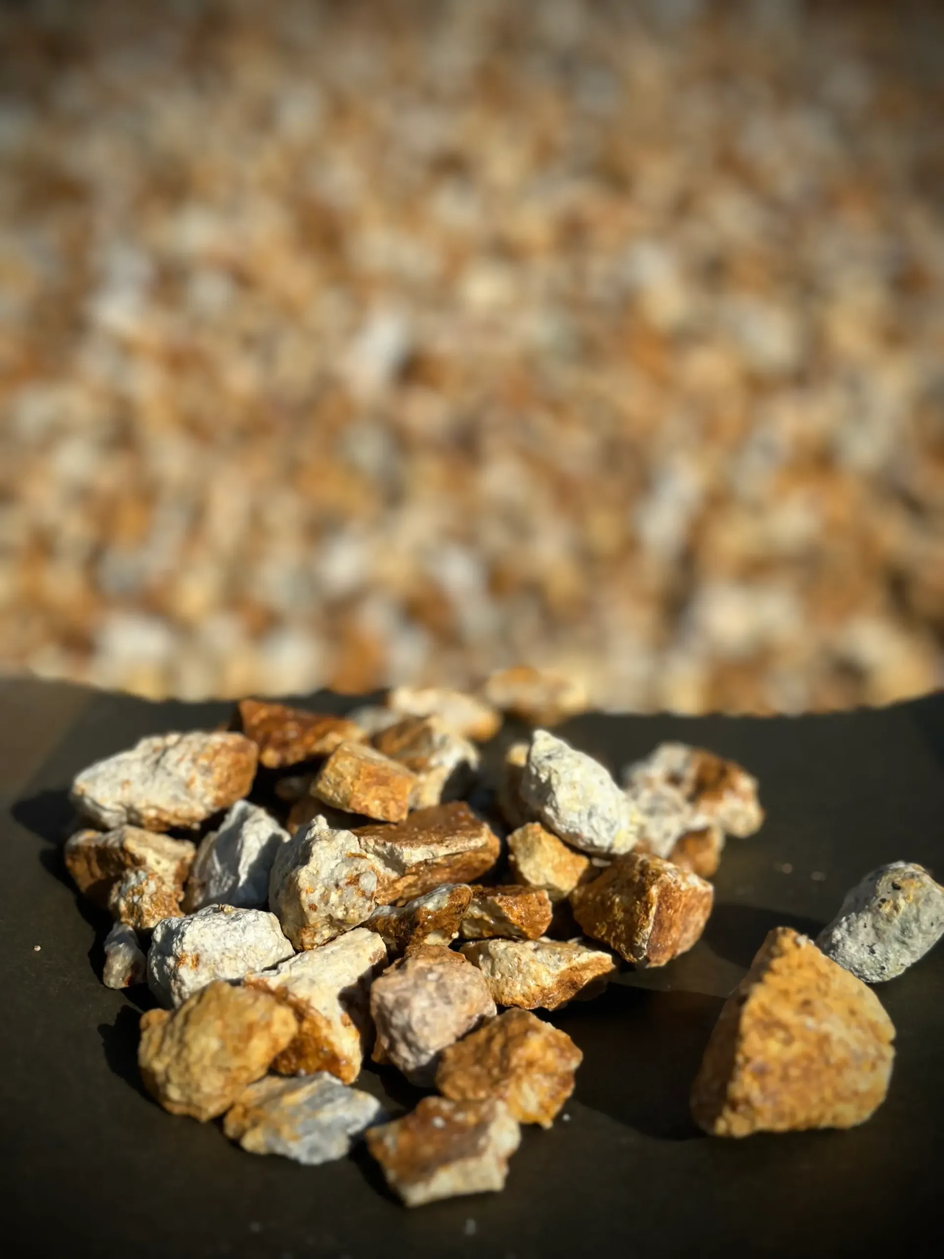 Close-up of brown and white gravel stones on a dark surface, with a blurred rock background