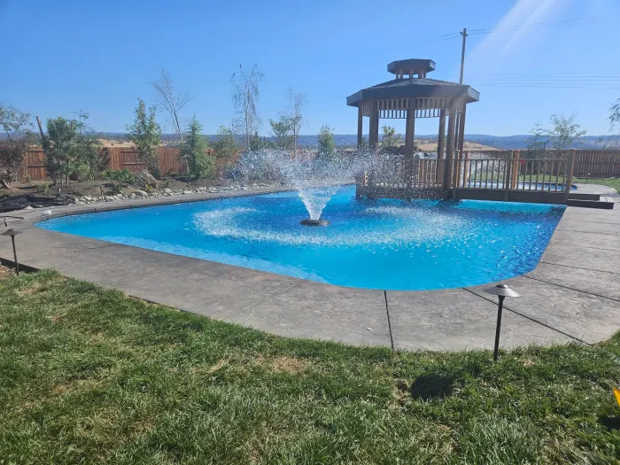 Outdoor pool with a water fountain and shaded gazebo on a sunny day