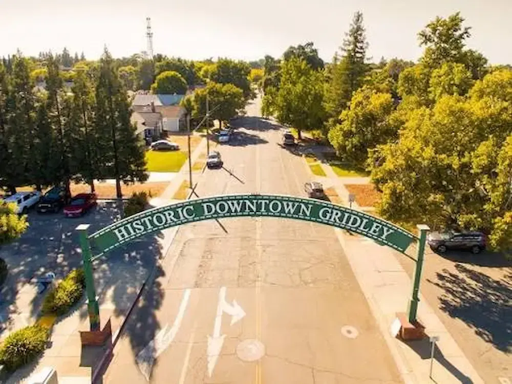 Historic downtown gridley arch over a sunlit street lined with trees and parked cars