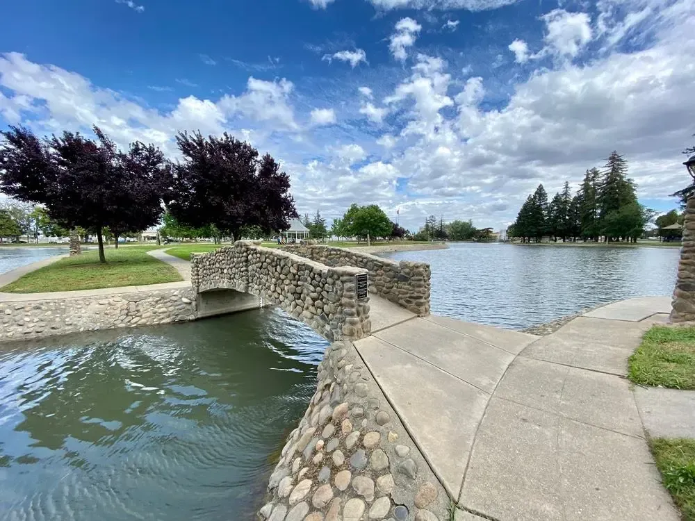 Stone footbridge over a pond in a park under a blue sky with clouds