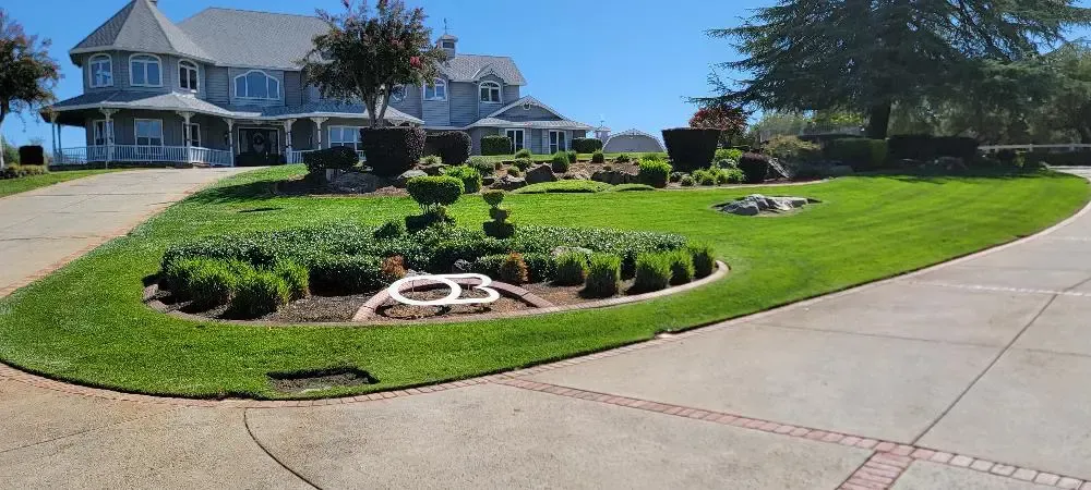 Large suburban house with landscaped lawn, flowerbeds, and a curved driveway on a sunny day