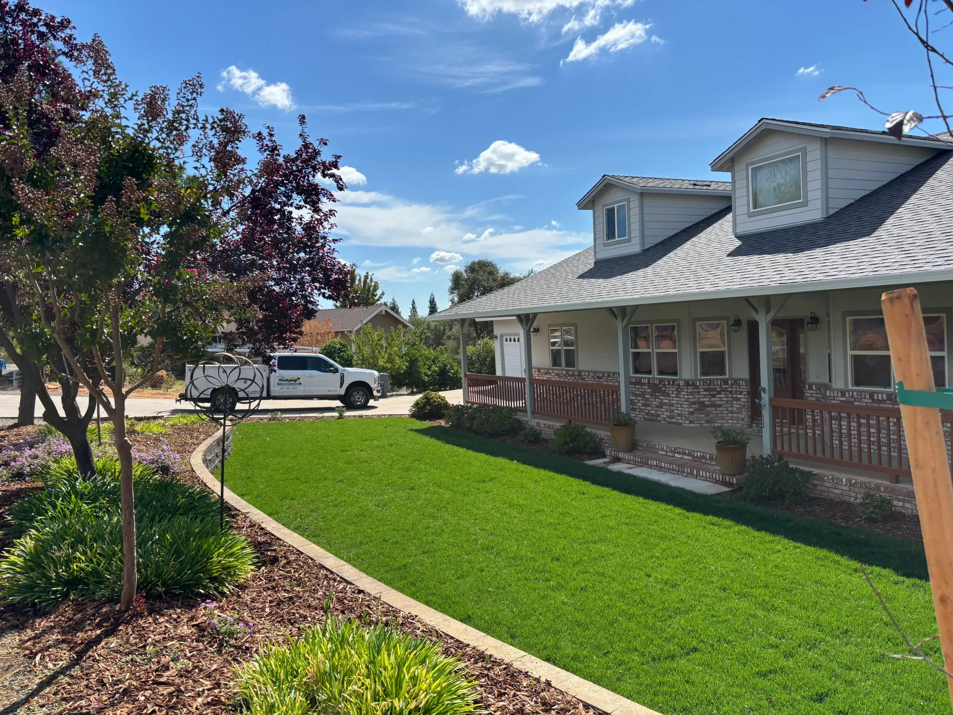 Brick house with a white porch and green lawn under a blue sky