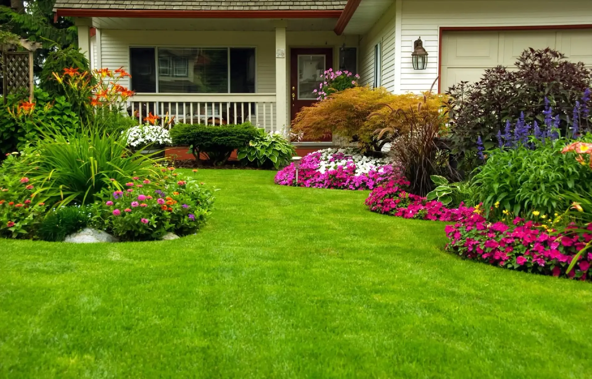Lush front yard with bright green lawn and colorful flowers in front of a house porch
