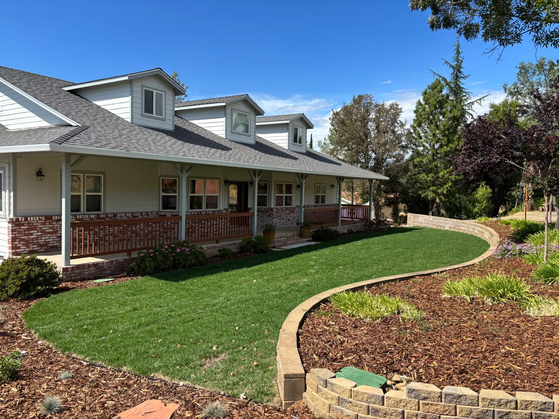 Landscaped front yard with curved walkway beside a brick house under a clear blue sky