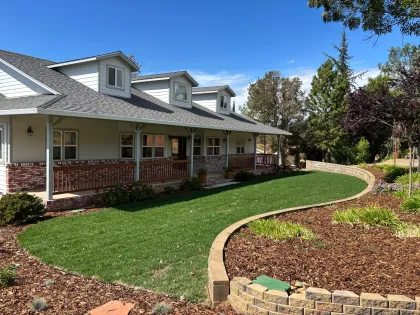 Front porch of a brick-and-siding house with a curved green lawn and landscaped garden beds