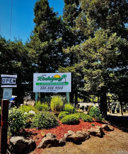Garden entrance sign with “OPEN” marker, green landscaping, and trees under a clear blue sky