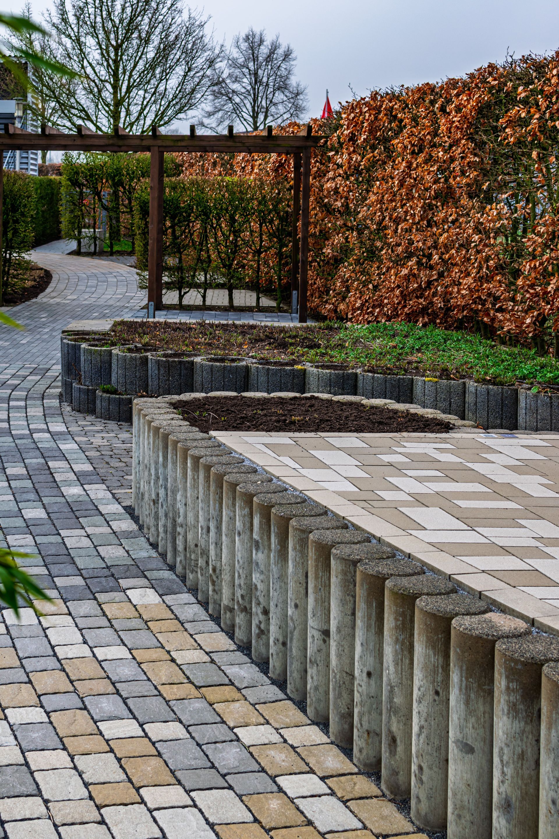 Curved stone walkway beside a raised planter and orange hedge in a landscaped garden