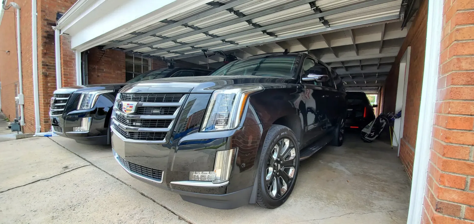 Two black Cadillac Escalades and a motorcycle parked in a garage.