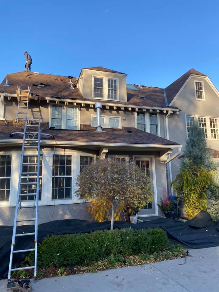 A man on a ladder is working on the roof of a house.
