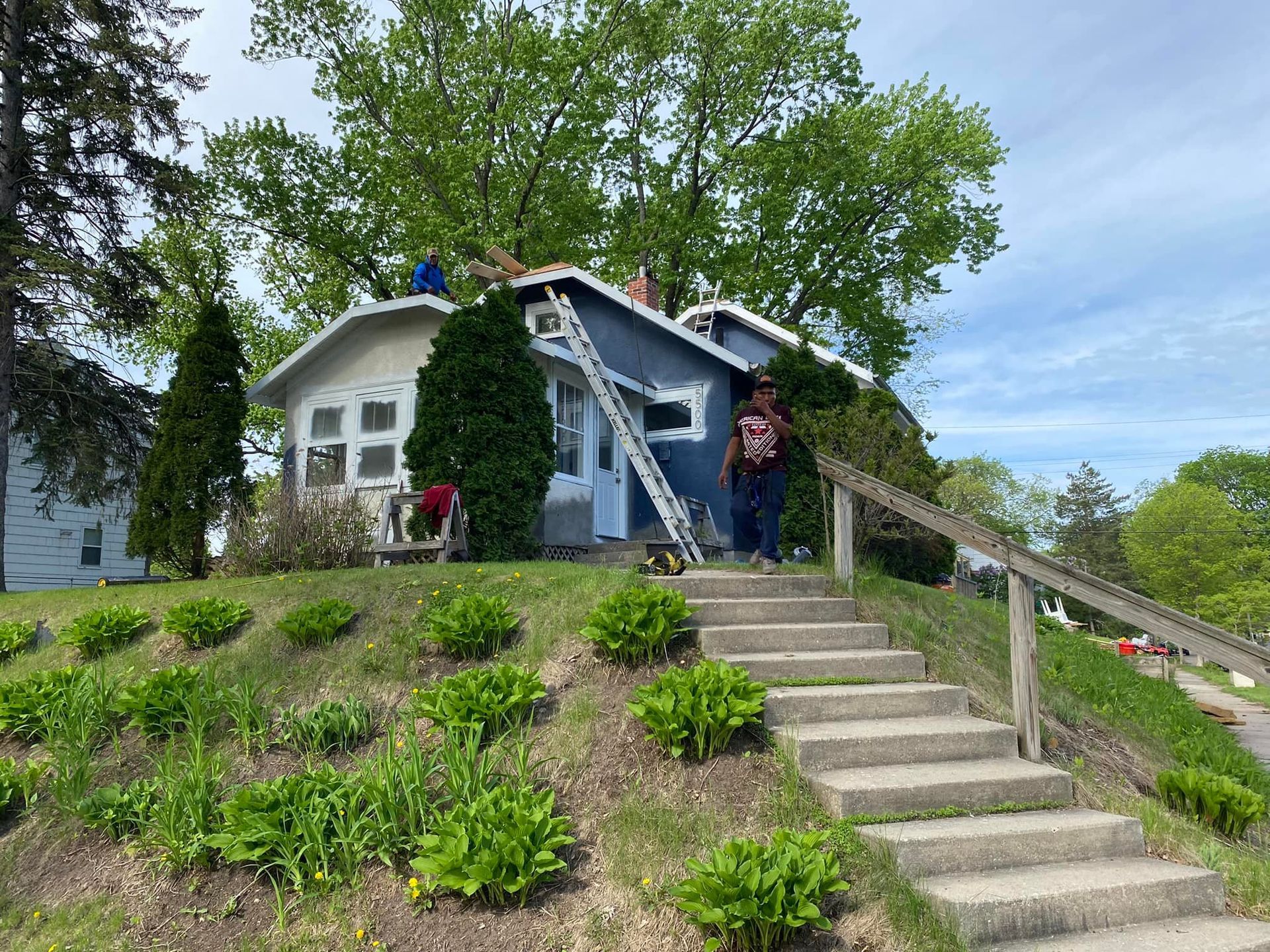 A man is standing on the roof of a house with a ladder.