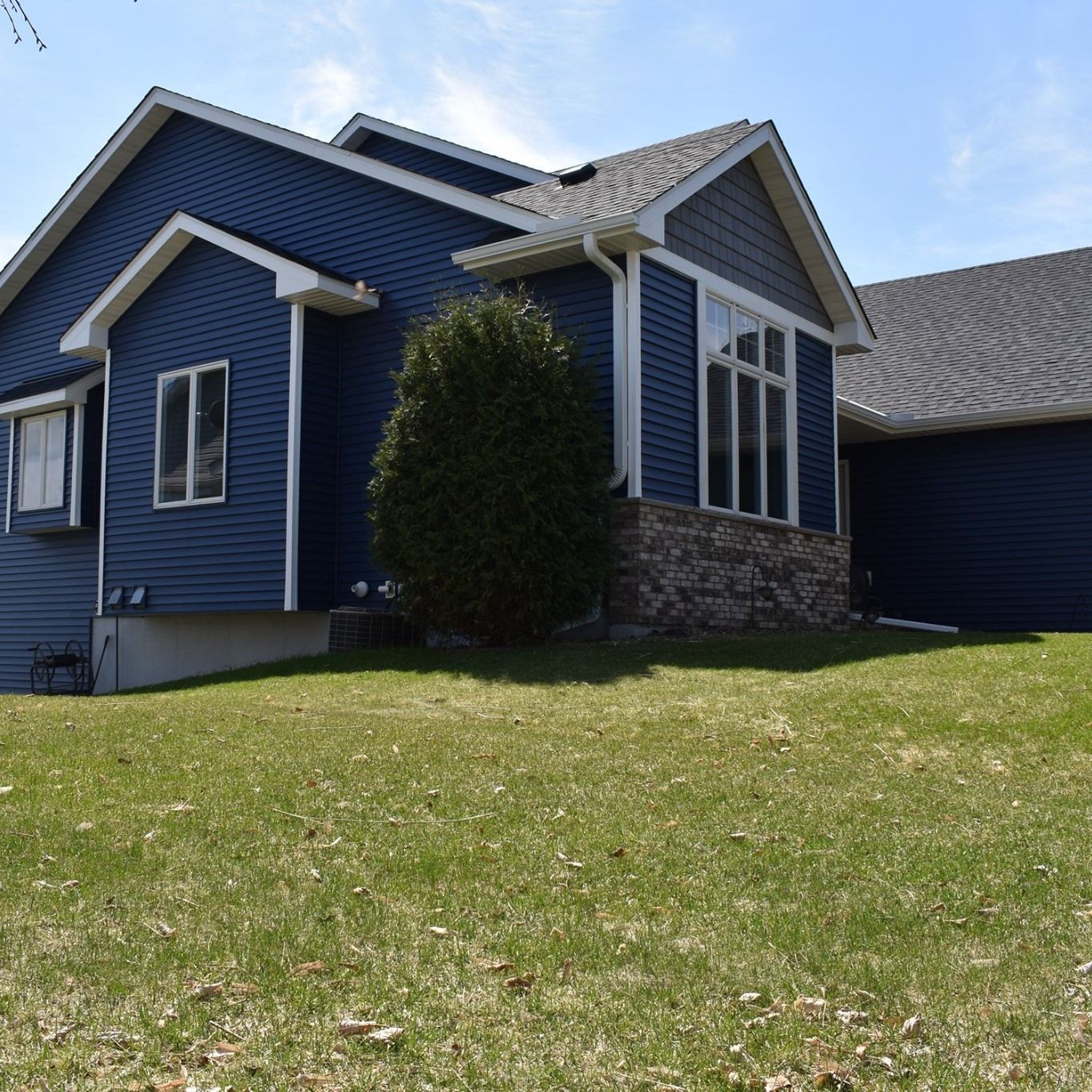 A blue house with white trim sits on a grassy hillside