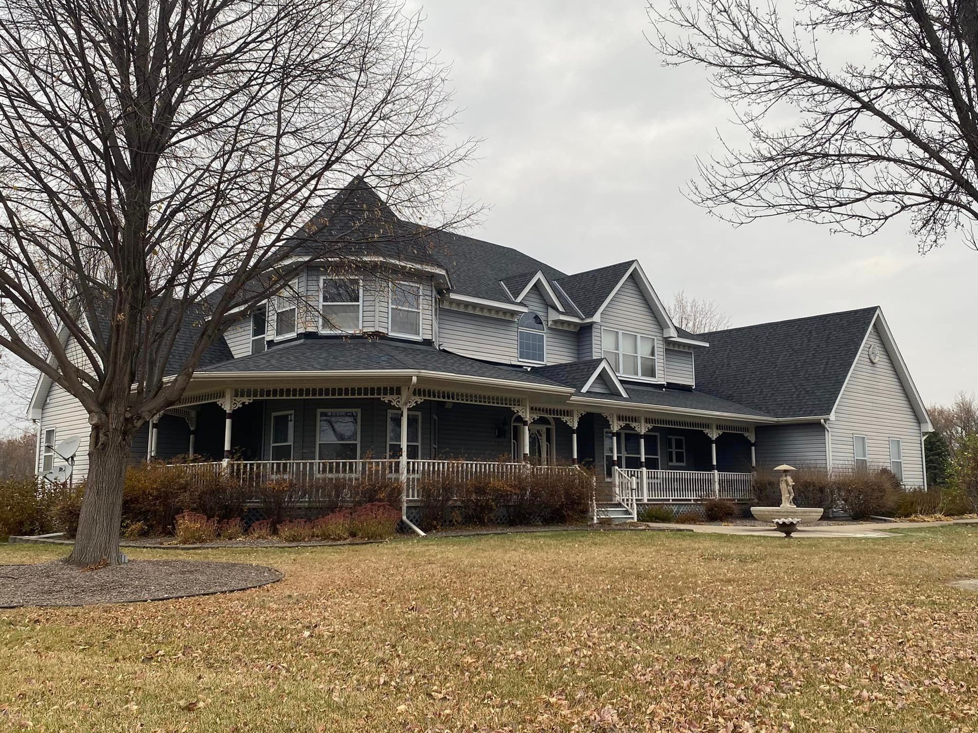 A large house with a large porch and a tree in front of it.