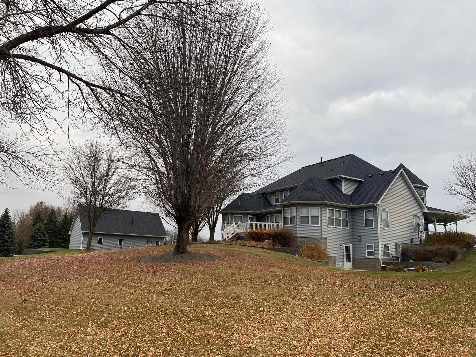 A large house is sitting on top of a hill with a tree in front of it.