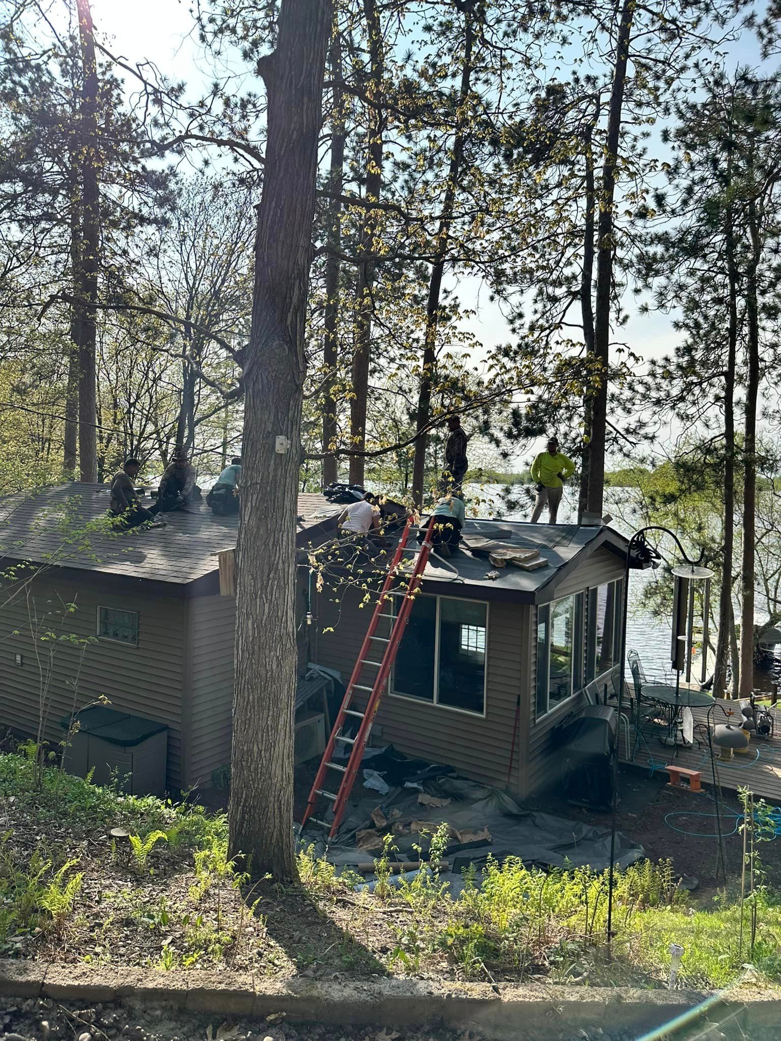 A group of people are working on the roof of a house in the woods.