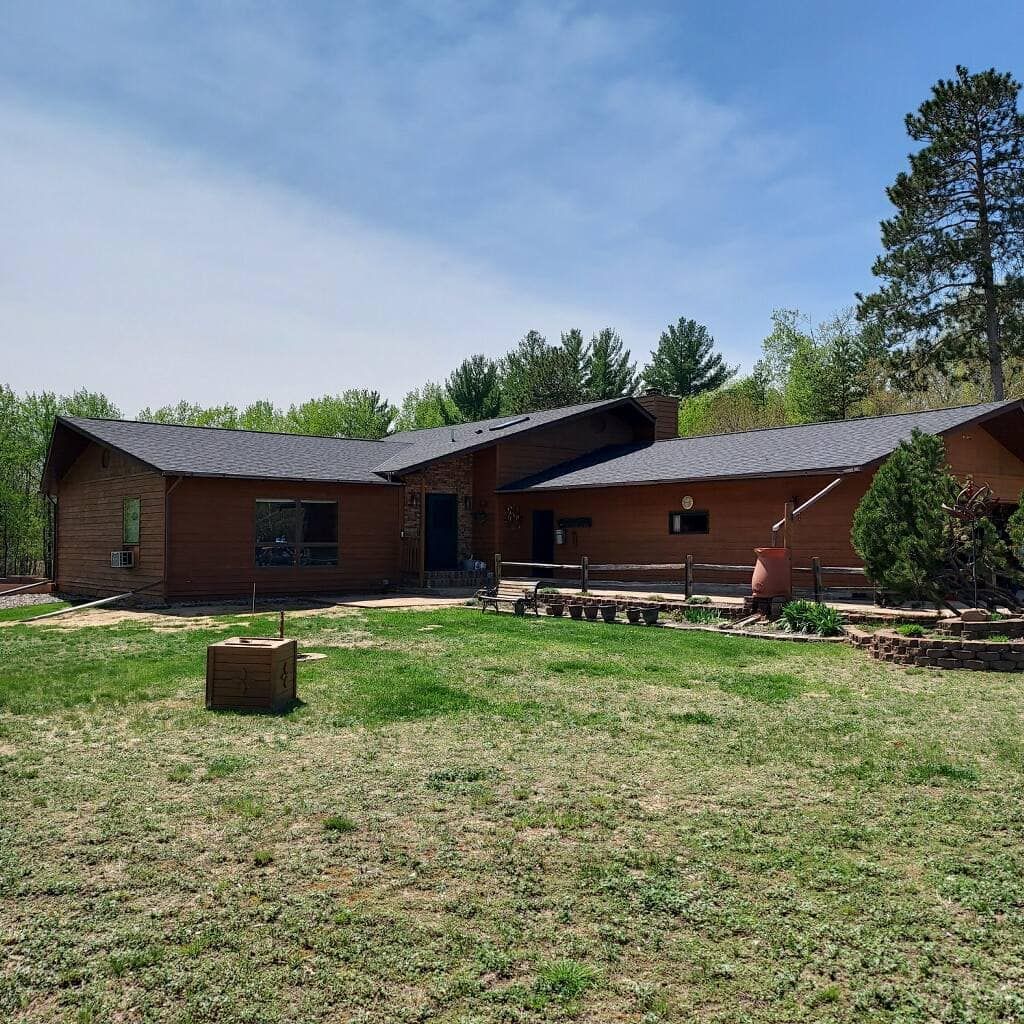 A large brick house with a gray roof sits in the middle of a lush green field.