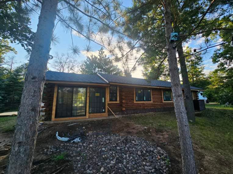 A log cabin with a sliding glass door is surrounded by trees.