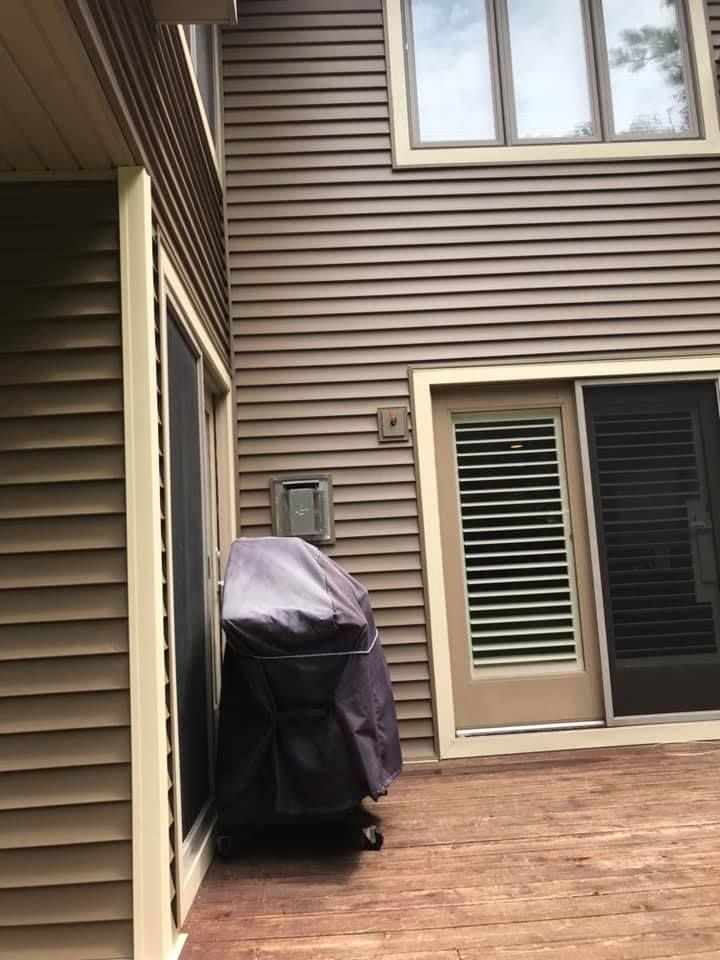 A grill is sitting on the side of a house next to a sliding glass door.