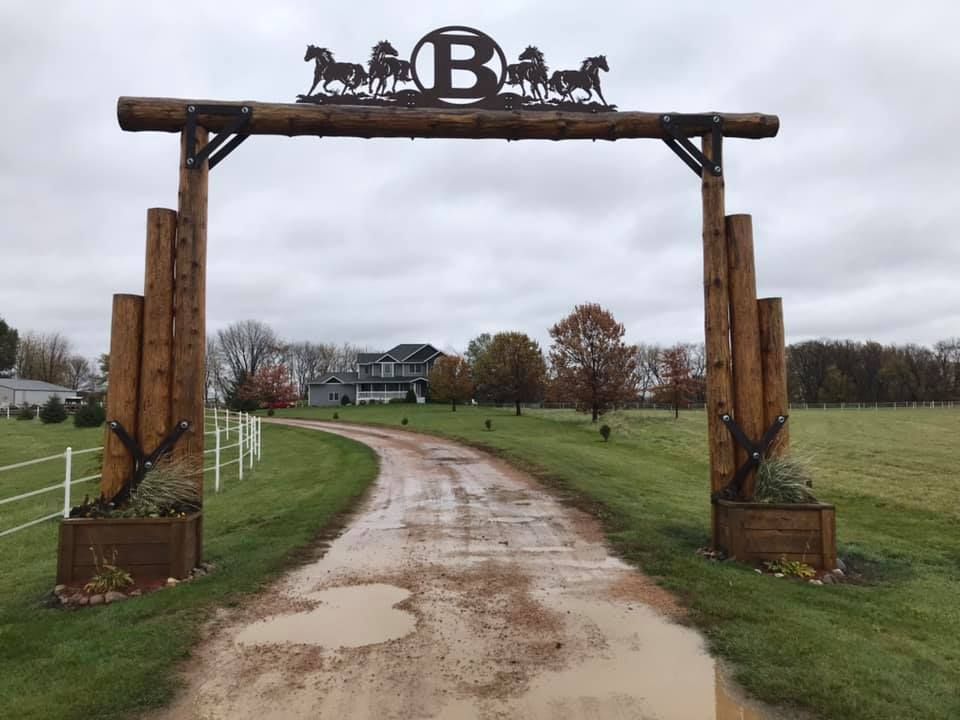 A dirt road with a wooden archway leading to a house.