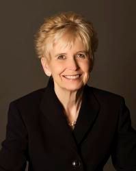 A woman in a black jacket is smiling for the camera.