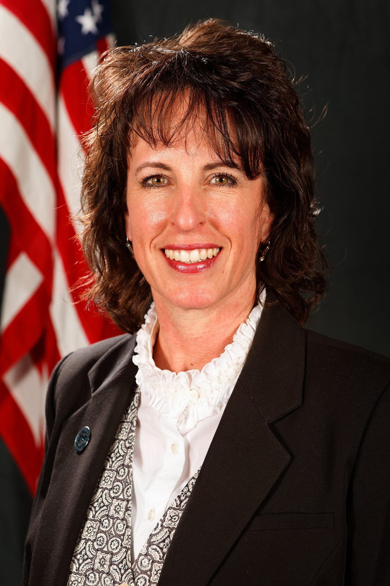 A woman in a suit is smiling in front of an american flag.