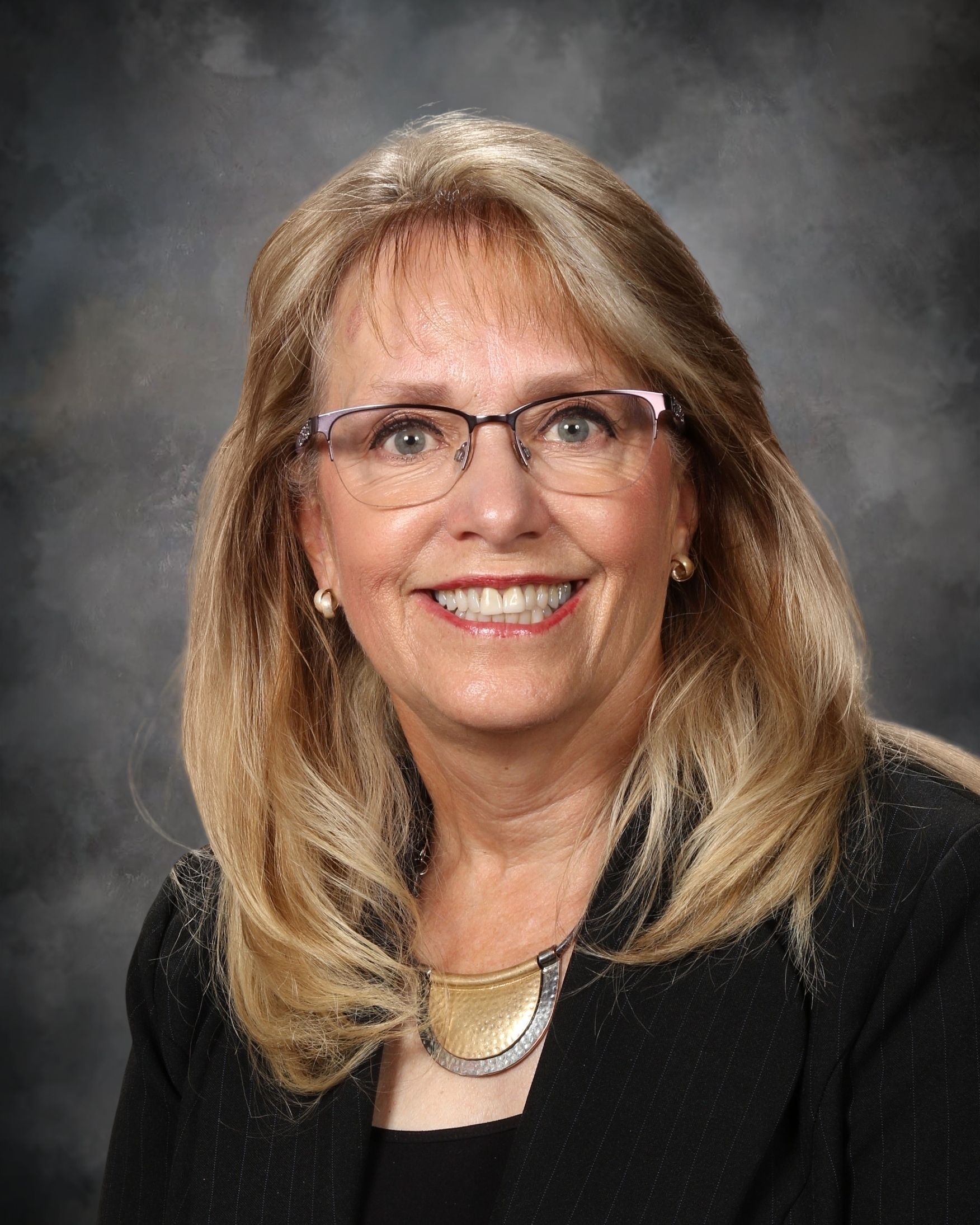 A woman in a suit is smiling in front of an american flag.