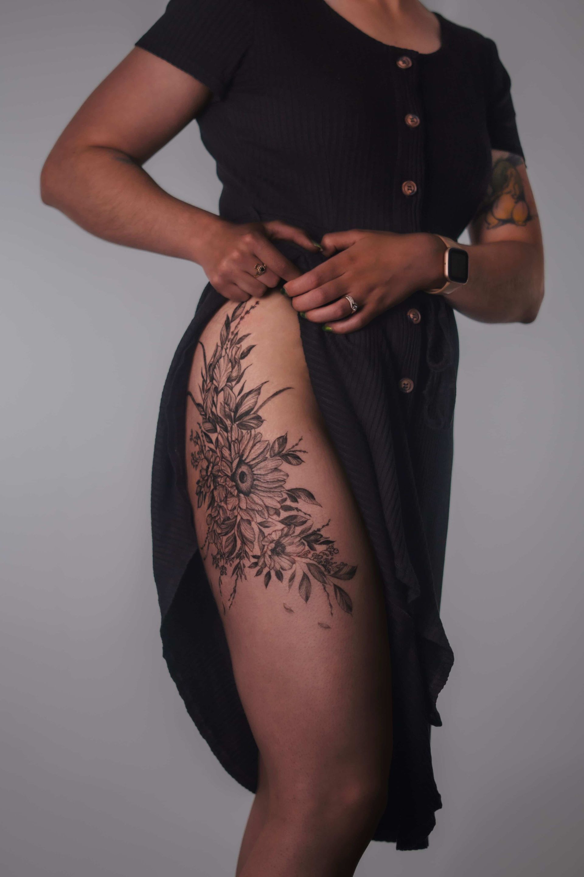 Woman in black dress, leg baring large floral tattoo.
