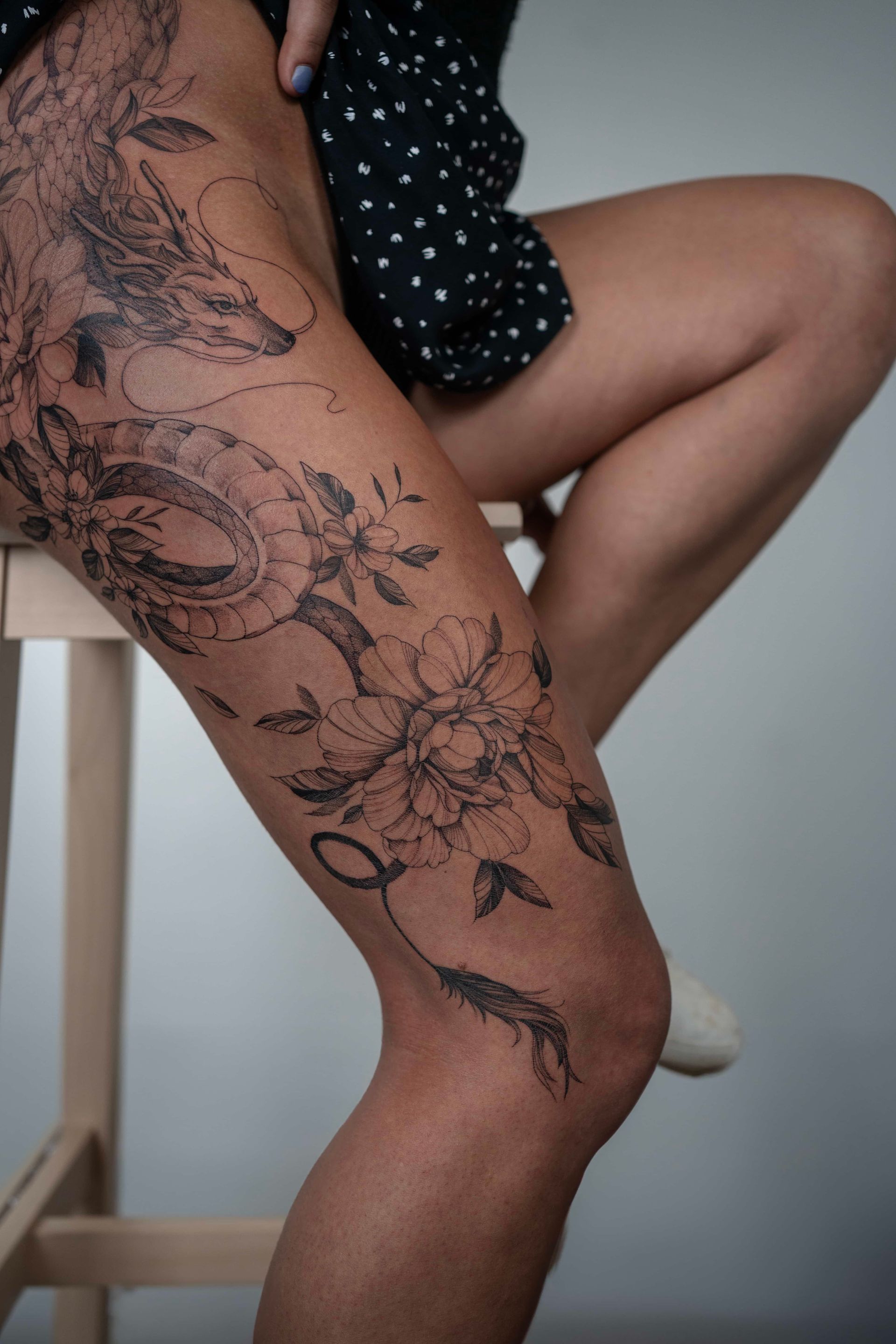 Leg with intricate black tattoo, floral and animal designs. Person seated with legs crossed.
