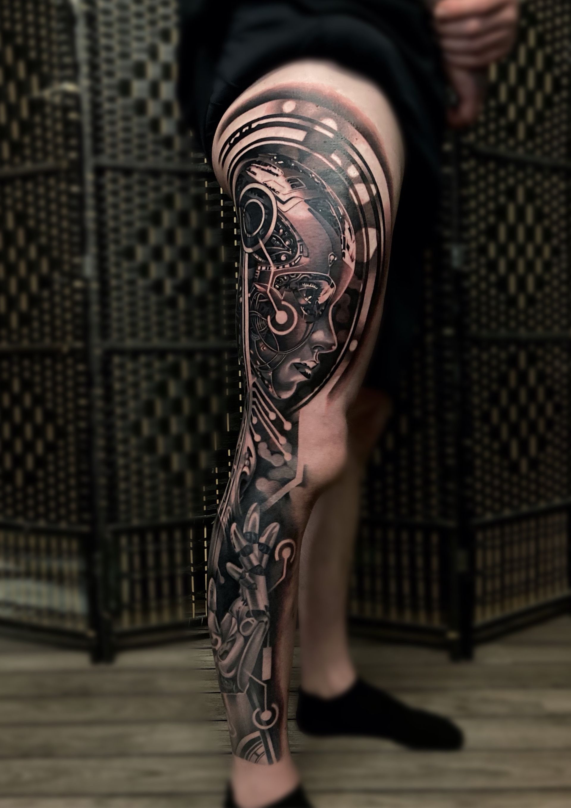 Leg tattoo featuring a detailed cyborg woman with interconnected circuitry and tech elements in grayscale.