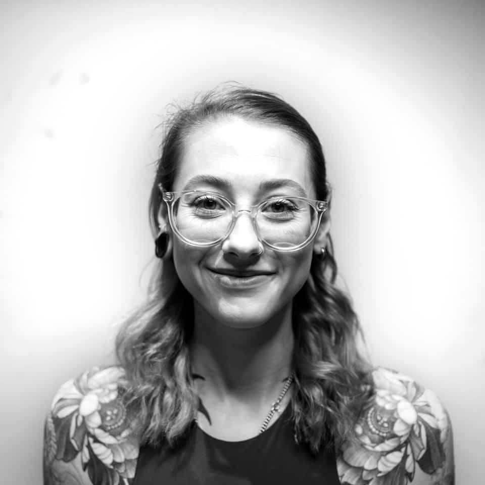 Woman with glasses and tattoos smiles.
