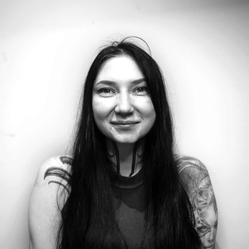Woman with long dark hair and tattoos, smiling.