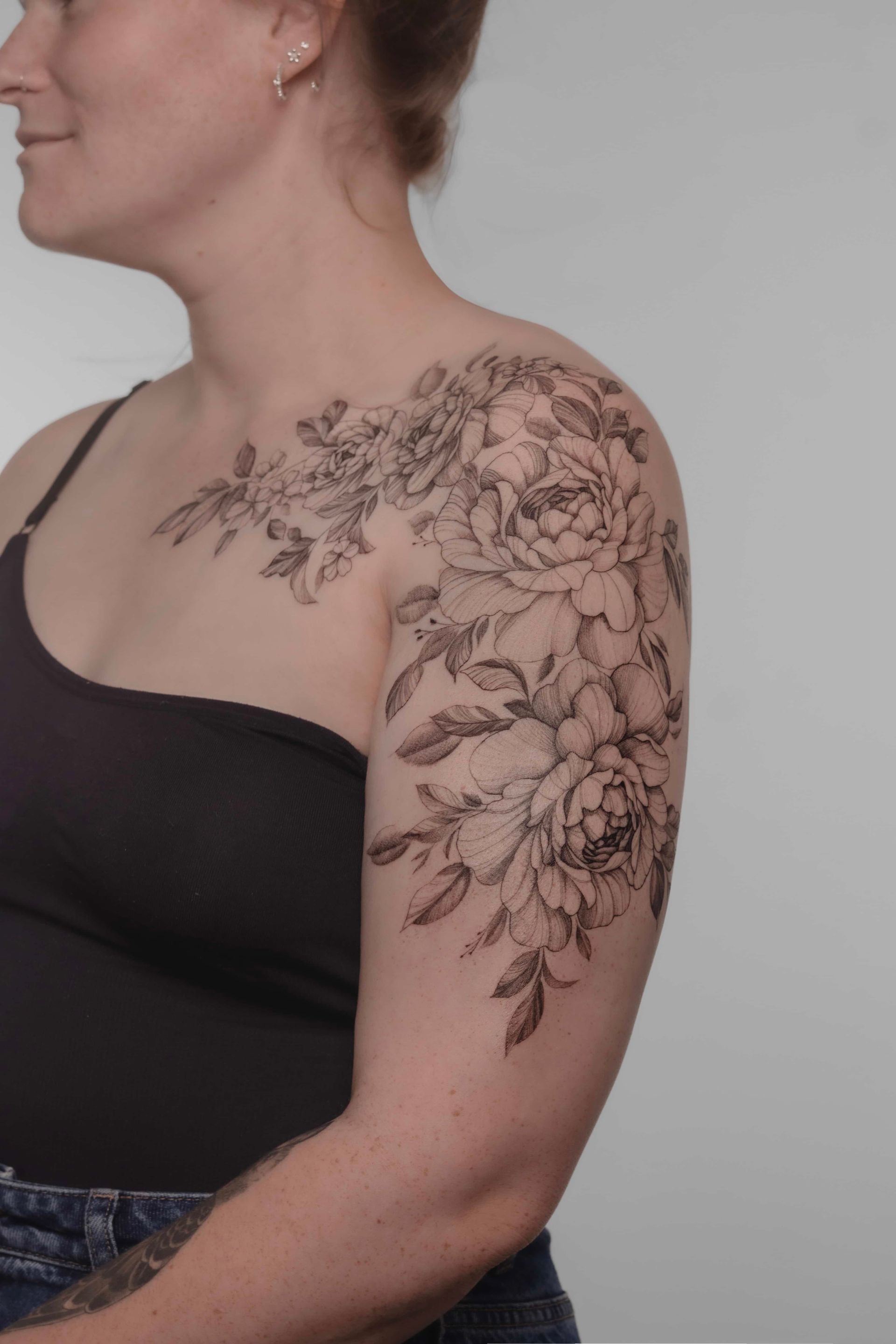 Woman with floral tattoo on shoulder and arm. She wears a black top and smiles slightly.
