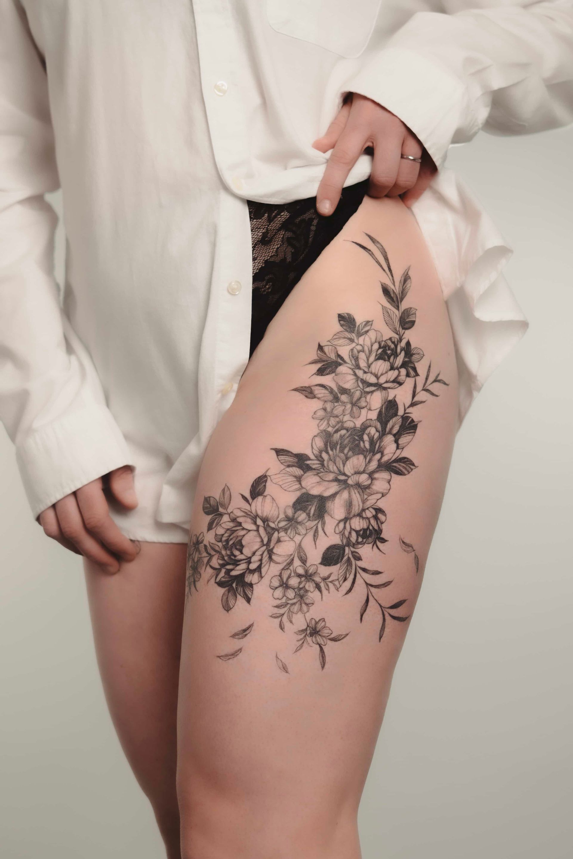 Thigh tattoo of a floral design. Person wearing white shirt, partially open, exposing the tattoo.