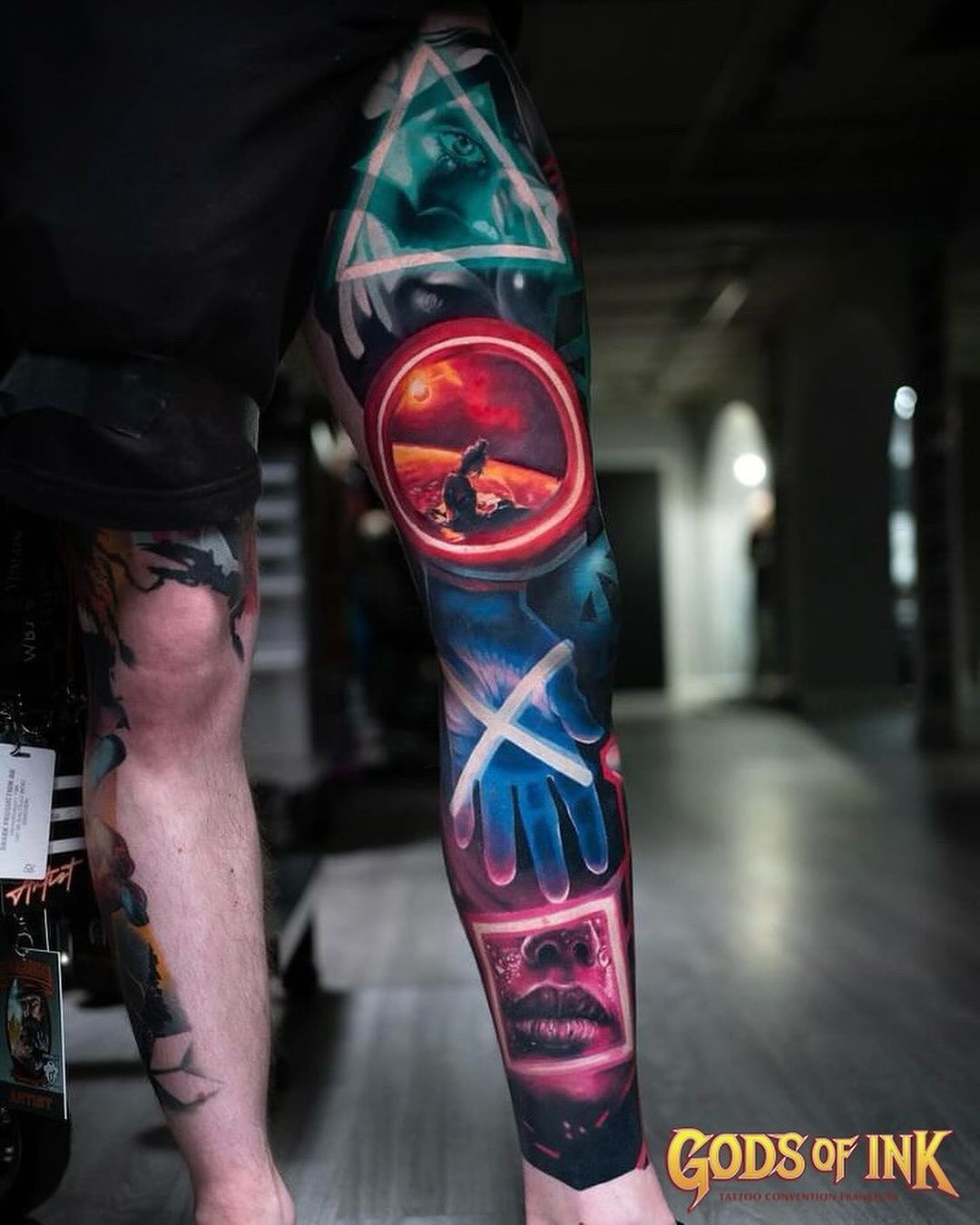 A leg tattoo featuring PlayStation controller symbols with a landscape scene in the circle button and a textured background.