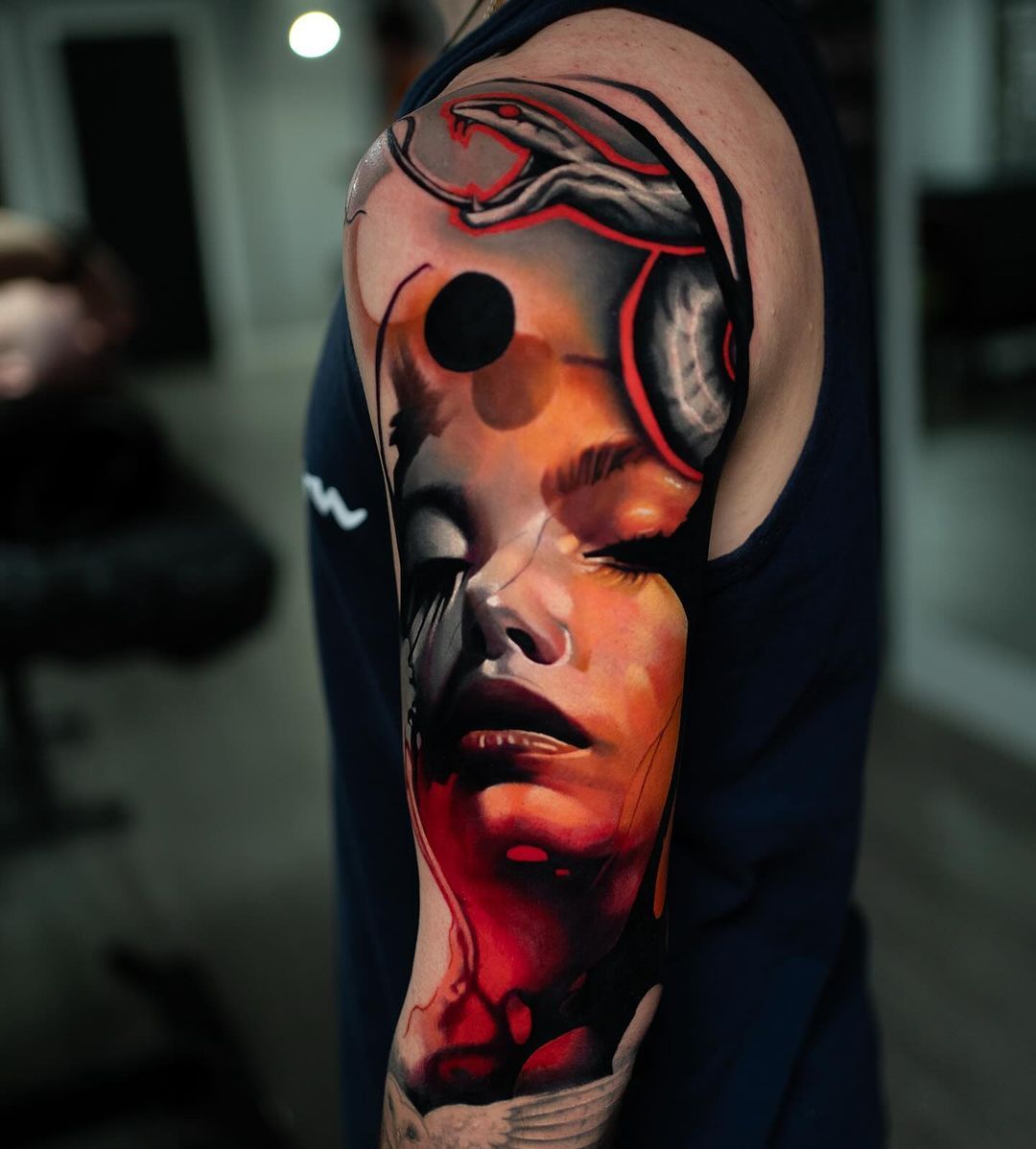 Colorful, abstract tattoo on an arm, featuring a woman's face with closed eyes and other geometric shapes