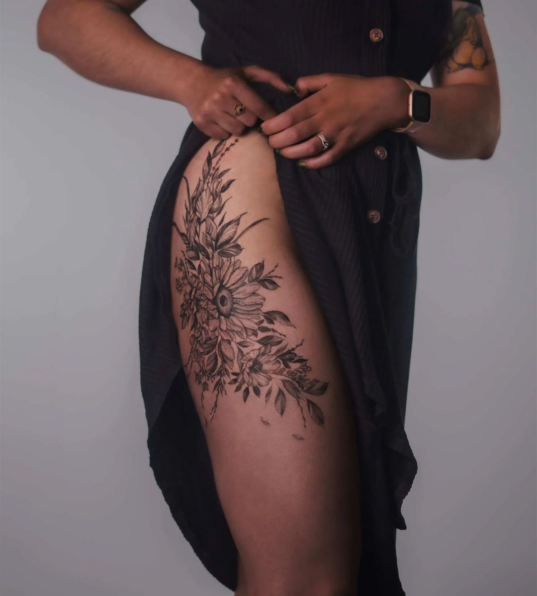 Woman lifting dress hem, revealing large floral tattoo on thigh.