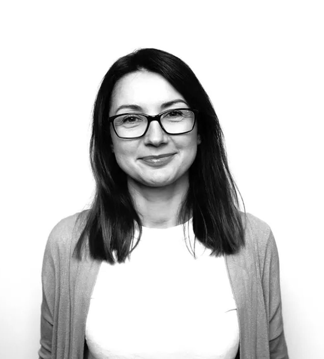 Woman with glasses smiling, wearing a cardigan over a white shirt, against a white backdrop.