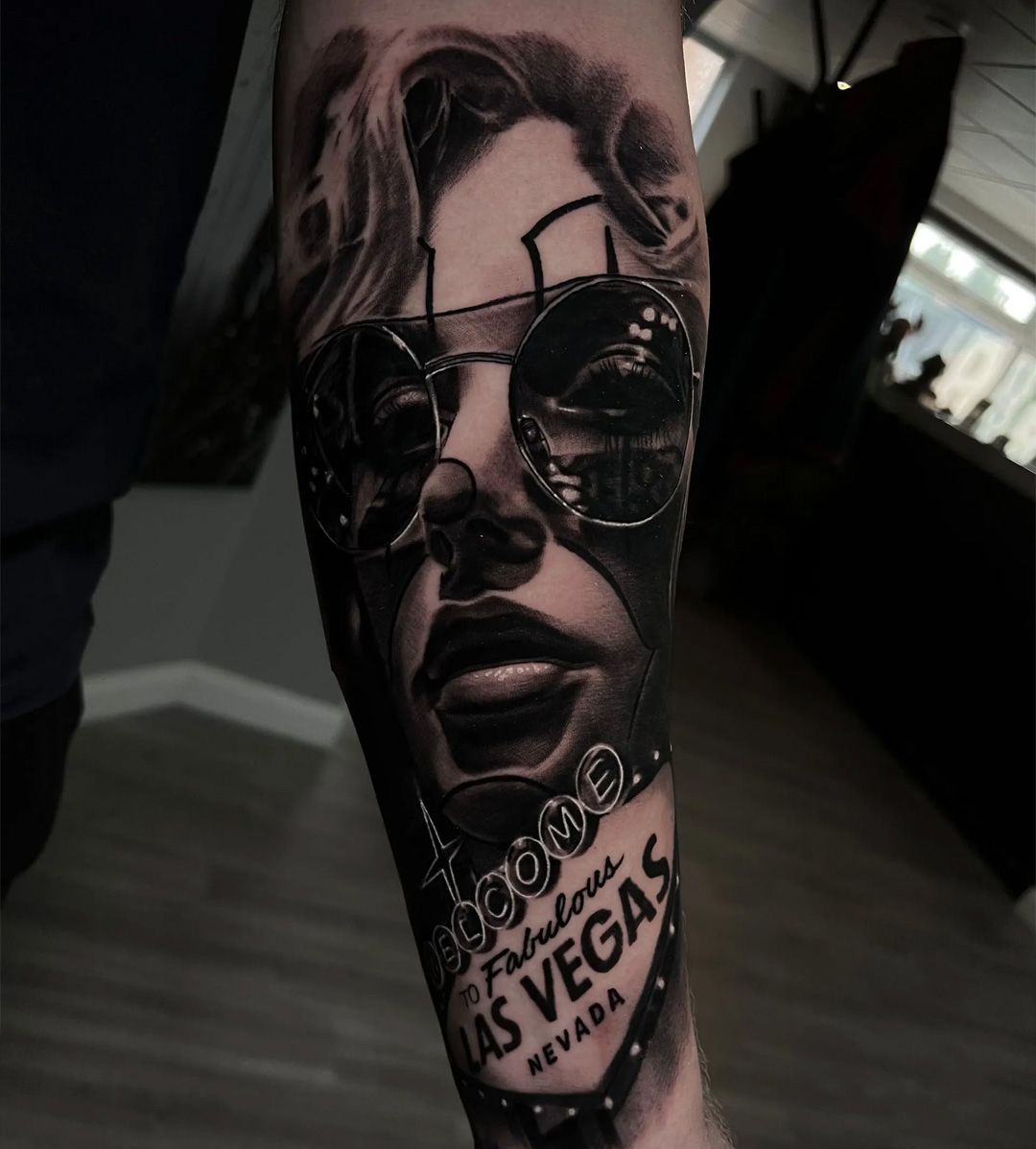 Black and white tattoo of a woman wearing sunglasses, with a 