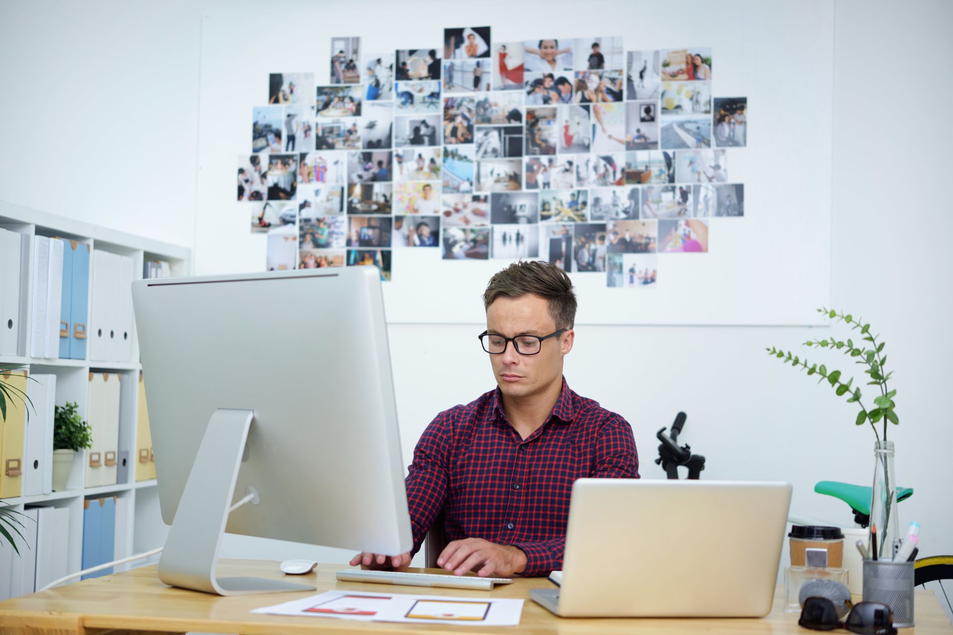A man is sitting at a desk in front of a computer and a laptop.