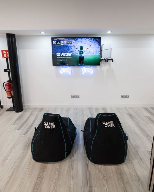 Dos bolsas de lona negras sobre un suelo alfombrado frente a un televisor montado en la pared en una habitación moderna.