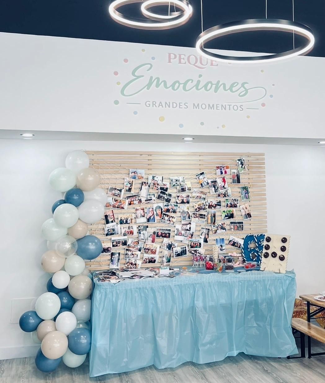Decoración para eventos con arco de globos, collage de fotos y mantel azul bajo luces de anillo brillantes.