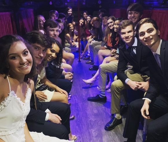 A group of people are sitting in a room with purple lights enjoying a Graduation Party with Party Bus Rentals in Austin.