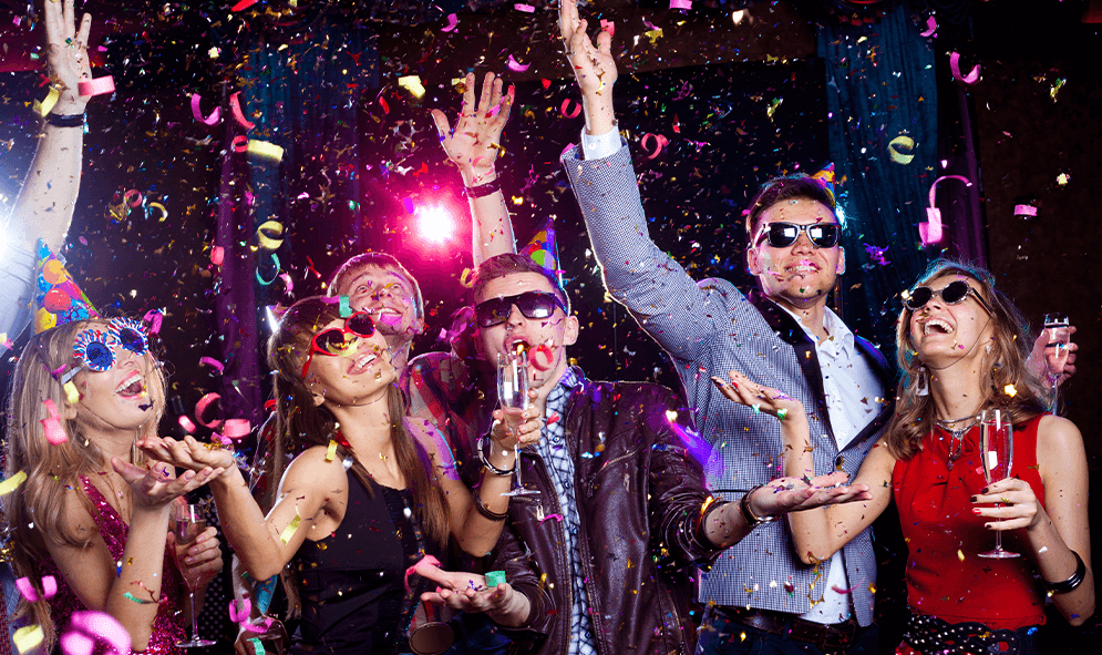 A group of people are dancing at a party and throwing confetti in the air.