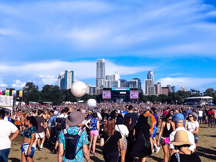 A crowd of people are walking in a field at a music festival.